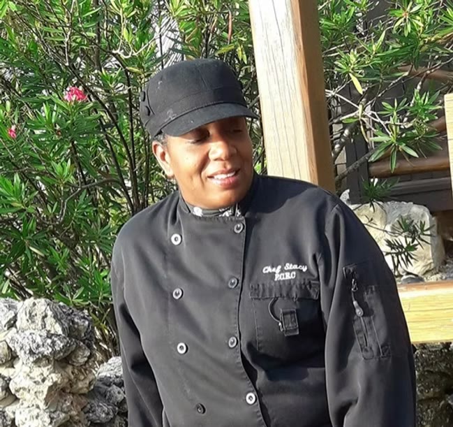 Chef Stacy Smith in a white chef coat beside fresh island seafood and herbs